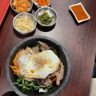 Bulgogi kimbop with spinach, pickled dicone, carrots, lettuce, with rice in hot stone bowl.