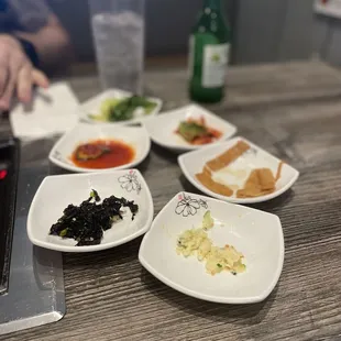 Banchan- Korean potato salad, seaweed salad, tofu strips, cucumber kimchi, kimchi, salad.