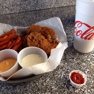 a basket of fried chicken, sweet potato fries, and a drink