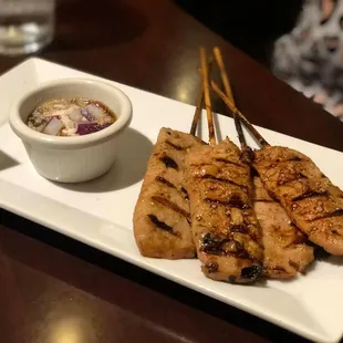 chicken skewers on a white plate with a side of dipping sauce