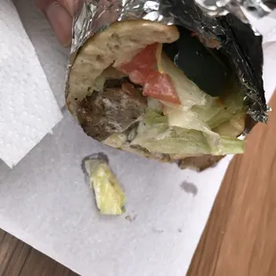 a hand holding a sandwich wrapped in foil