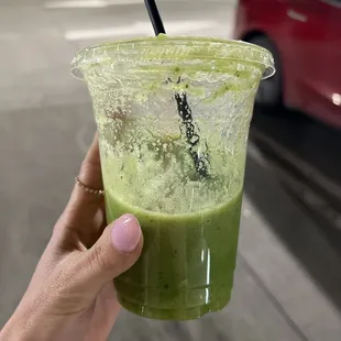 a hand holding a cup of green juice