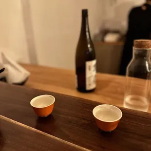 two cups of tea on a table with a bottle of wine in the background