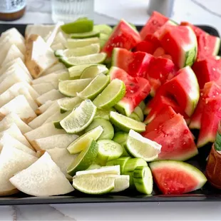 a platter of sliced watermelon, limes, and cucumbers