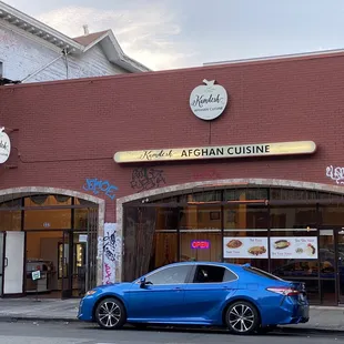 a blue car parked in front of a restaurant