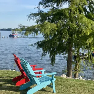 a pair of adirondacks sitting on the grass by the water