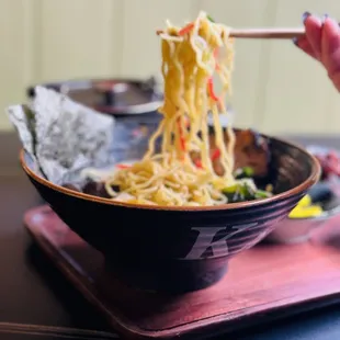 a person holding chopsticks over a bowl of ramen