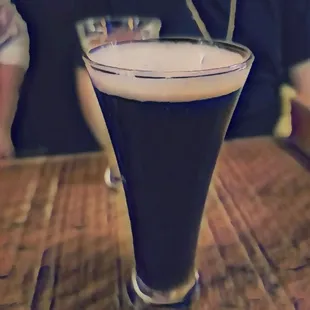 a glass of dark beer on a wooden table