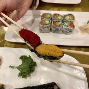 a person holding chopsticks over a plate of sushi