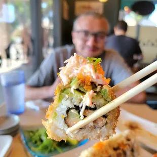 a man sitting at a table with a plate of sushi and chopsticks