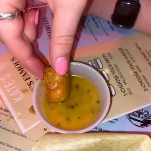 a person dipping a hot dog into a bowl of mustard