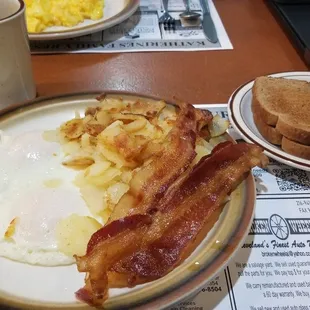 Eggs over easy, bacon, potatoes and wheat toast