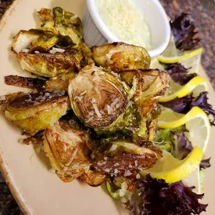 a plate of roasted brussel sprouts with lemon wedges