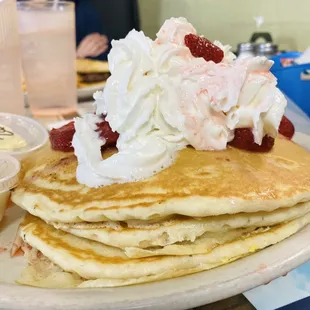 A three stack of pancakes with a mountain of whip cream and strawberries from Katie&apos;s diner