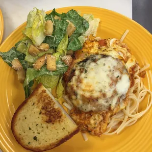 Homemade eggplant Parmesan on a bed of pasta with garlic bread and fresh Caesar salad.