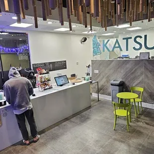 INTERIOR: A wide-angle photo of the cafe floor. Customers can order from the kiosks and wait with others. Benches &amp; tables in picture.