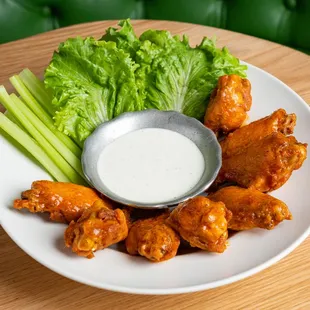 a plate of chicken wings with ranch dressing and celery