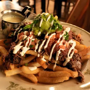 Loaded Birria Fries: french fries, shredded cheese, braised beef, salsa roja, crema guacamole, pico de gallo, Kavas Queso ($18).