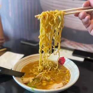 a person holding chopsticks over a bowl of ramen