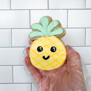 a hand holding a decorated pineapple cookie