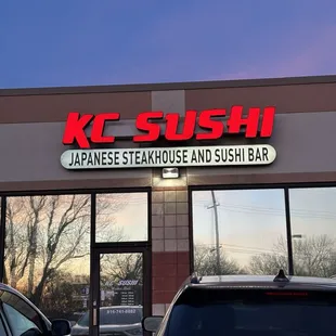 two cars parked in front of a japanese steakhouse and sushi bar