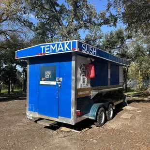 a small blue food truck parked in a dirt lot