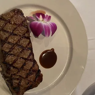 a steak on a plate with sauce and a flower