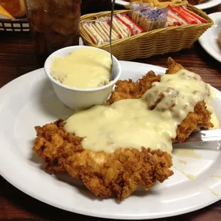 Country fried chicken breast with cream gravy and a side of rice topped with gravy.