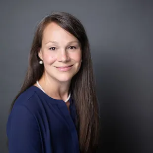 Professional studio headshot with grey background, navy blouse