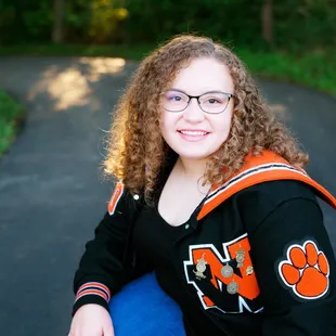 Senior girl at senior portrait session in the park, letter jacket and jeans