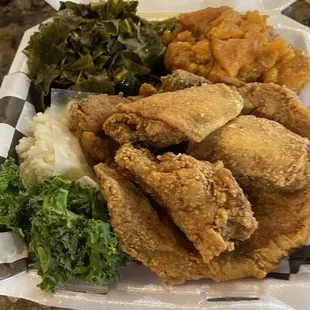 Fried chicken wings and fried pork chop on a bed of rice with collards and yams.