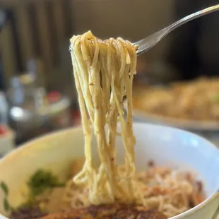 a bowl of noodles being held by a fork