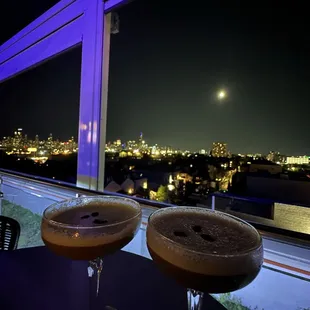 two cocktails on a table with a view of the city