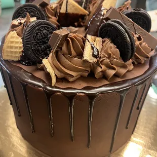 Cocoa Loco is a decadent chocolate cake with a chocolate buttercream and chocolate ganache drip. Topped with chocolate candies and cookies.