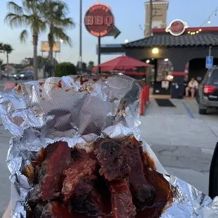 ows a hand holding a foil wrap of ribs