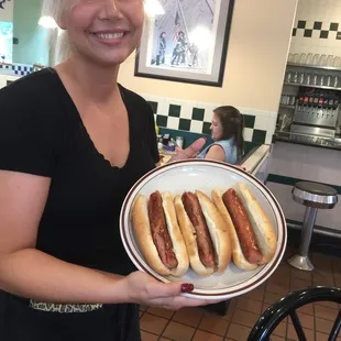 a woman holding a plate of hot dogs