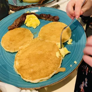 a blue plate with pancakes, bacon, eggs, and sausage