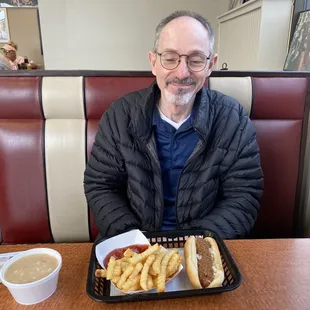 a man sitting at a table with a tray of hot dogs and french fries