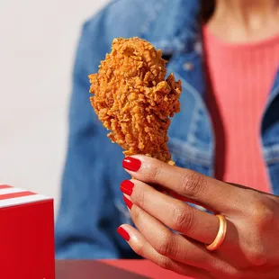 a woman holding a fried chicken on a stick