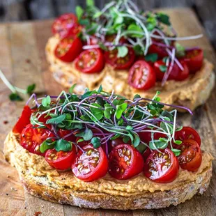 two pieces of bread topped with tomatoes and sprouts