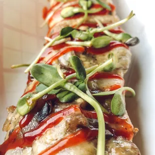 a long piece of food with sauce and sprouts