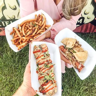 a woman holding two trays of hotdogs and french fries