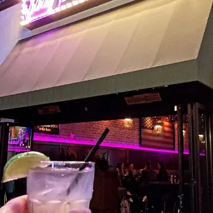 a hand holding a cocktail outside of a restaurant