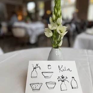 A handmade bud vase with our Kiln postcard with a blurred image of our main dining room.