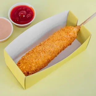 a corn dog in a box with dipping sauces