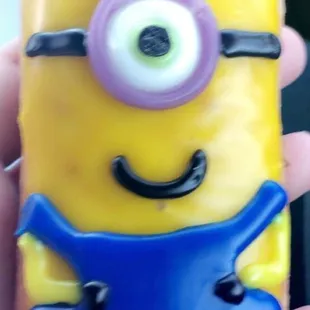 a hand holding a donut decorated like a minion