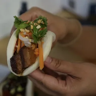 a person holding a bun with meat and vegetables