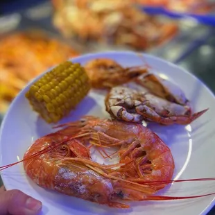 a person holding a plate of shrimp and corn