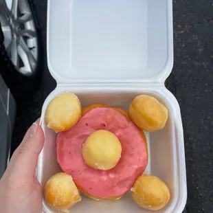 a person holding a container with a donut in the shape of a flower
