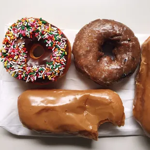 Two maple bars, one blueberry glazed donut, and one chocolate sprinkle donut.